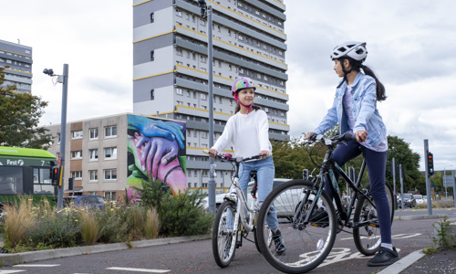 Two girls on bikes using a segregated cycle path next to a busy road