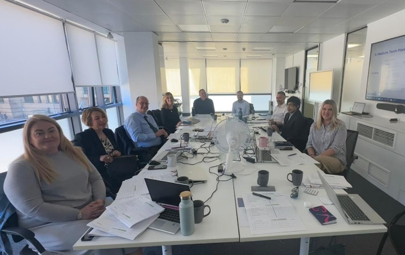 Members of the board sitting at a table in a meeting room with laptops and papers
